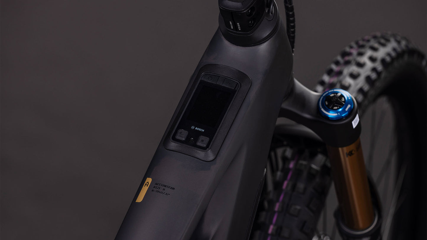 Nahaufnahme des CUBE Stereo Hybrid ONE77 HPC AT 800 carbon'n'gold 2026 E-MTB-Rahmens mit einem im Oberrohr integrierten Bosch-Bedienfeld und einer Federgabel mit blauem Einstellknopf.