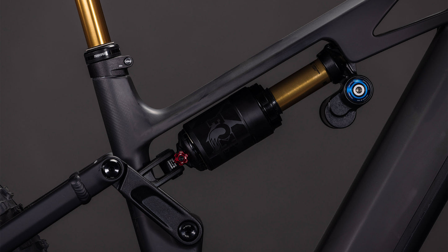 Nahaufnahme des CUBE Stereo Hybrid ONE77 HPC AT 800 carbon'n'gold 2026 mit seinem mattgrauen Carbon-Rahmen, dem hinteren Federbein, der Anlenkung und den goldenen und schwarzen Komponenten, die für Big-Mountain-Fahrten entwickelt wurden.