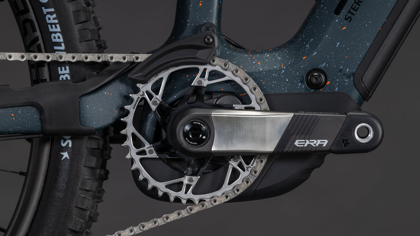 Nahaufnahme des Antriebs am CUBE Stereo Hybrid ONE77 HPC SLT 800 galaxy'n'orange 2026 mit Kurbelarm, Kettenblatt und Kette. Das ERA-Logo ist auf dem Kurbelarm zu sehen; das Fahrrad hat eine dunkle, gesprenkelte Lackierung für Big-Mountain-Performance.