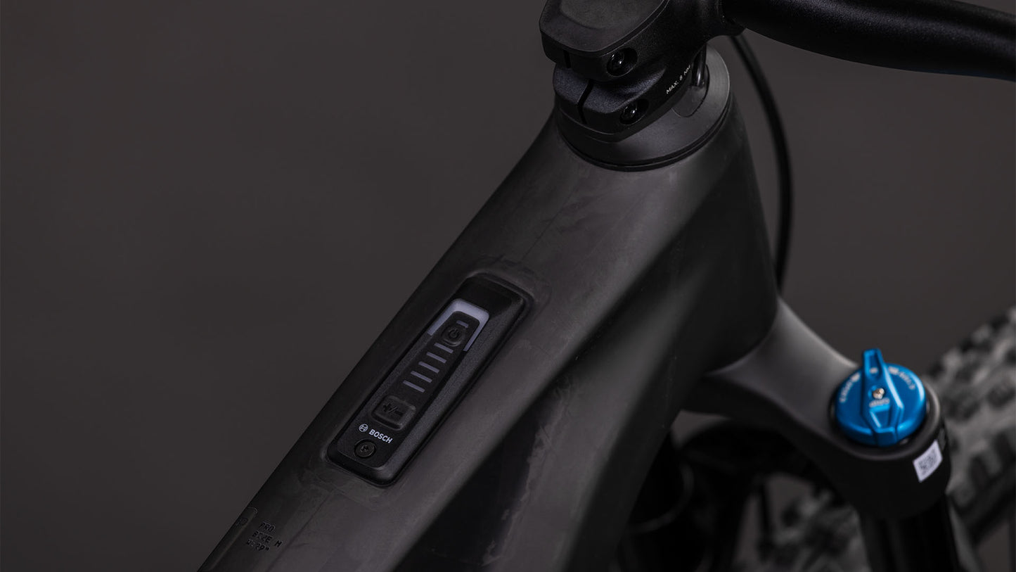 Nahaufnahme des Carbon-Oberrohrs des CUBE AMS Hybrid ONE44 C:62 Pro 400X blackline 2026. Zu sehen sind ein Bosch-Bedienungsdisplay mit Leistungs- und Batterieanzeige am Lenker und ein blauer Gabel-Einstellknopf vor dunklem Hintergrund.