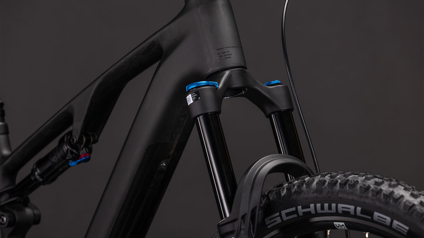 Nahaufnahme der vorderen Federgabel des CUBE AMS Hybrid ONE44 C:62 Pro 400X blackline 2026 mit blauen Einstellknöpfen und Schwalbe-Reifen. Der dunkle Hintergrund unterstreicht den C:62 Carbon-Rahmen und die hochwertigen Komponenten für beste Trail-Performance.