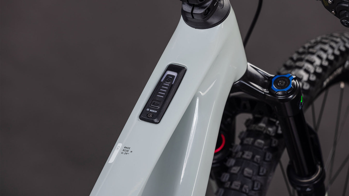 Nahaufnahme des CUBE AMS Hybrid ONE44 C:62 Race 400X reedbeige'n'black 2026 Rahmens von CUBE, die das Bosch-Bedienfeld und die Batterieanzeige auf dem Oberrohr mit einem Bosch SX Motor zeigt. Die vordere Federgabel und der Reifen sind im Hintergrund zu sehen.