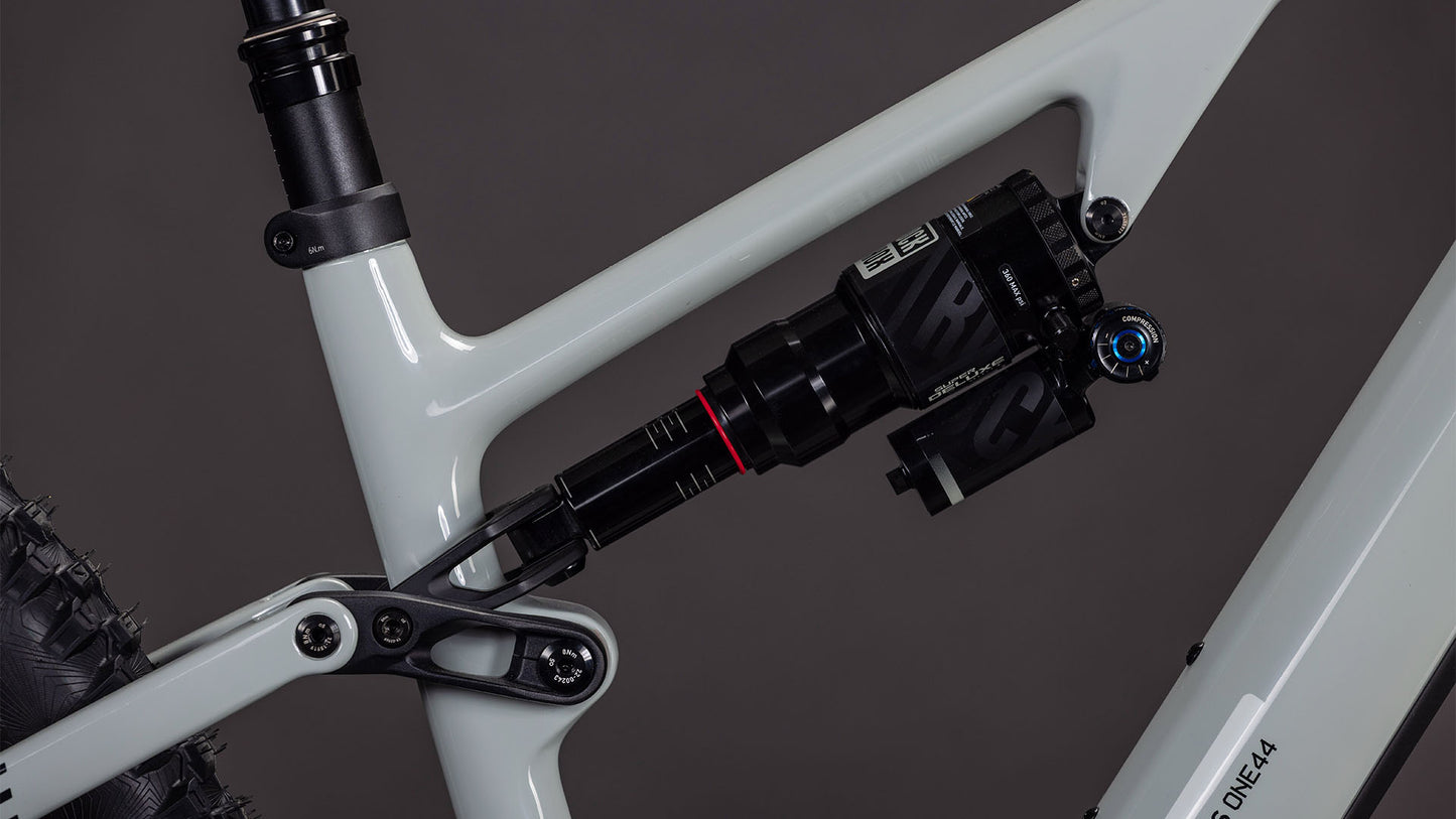 Nahaufnahme der Hinterradaufhängung, des Stoßdämpfers und des Hinterrads des CUBE AMS Hybrid ONE44 C:62 Race 400X, die den fortschrittlichen C:62 Carbonrahmen in schilfbeige'n'black vor einem dunklen Hintergrund zeigt.