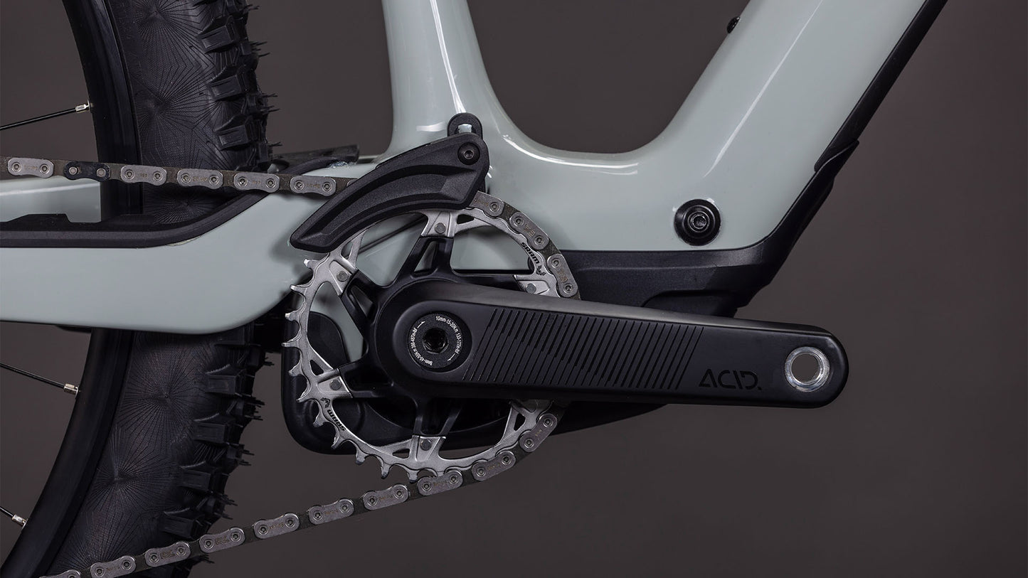 Nahaufnahme der Bosch SX-Motor-Kurbelgarnitur, des Kettenblatts und der Kette am C:62 Carbon-Rahmen des 2026 CUBE AMS Hybrid ONE44 C:62 Race 400X reedbeige'n'black, mit dem Profil des Hinterreifens und der Kettenstrebe vor dunklem Hintergrund.