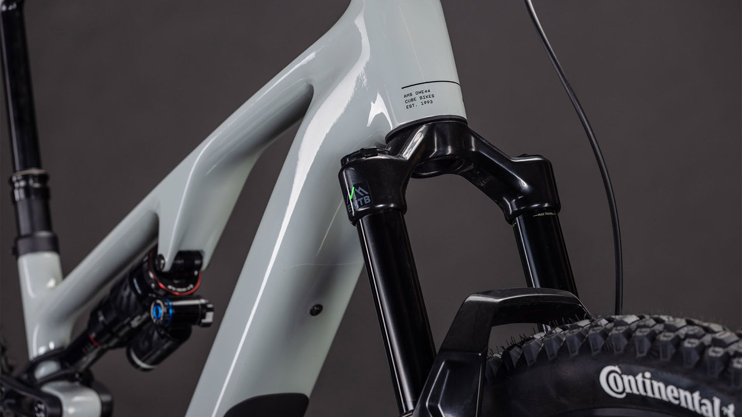 Nahaufnahme eines CUBE AMS Hybrid ONE44 C:62 Race 400X reedbeige'n'black 2026 Mountainbike-Rahmens mit Bosch SX Motor, Federgabel, C:62 Carbonrahmen und Continental-Vorderreifen vor dunklem Hintergrund.