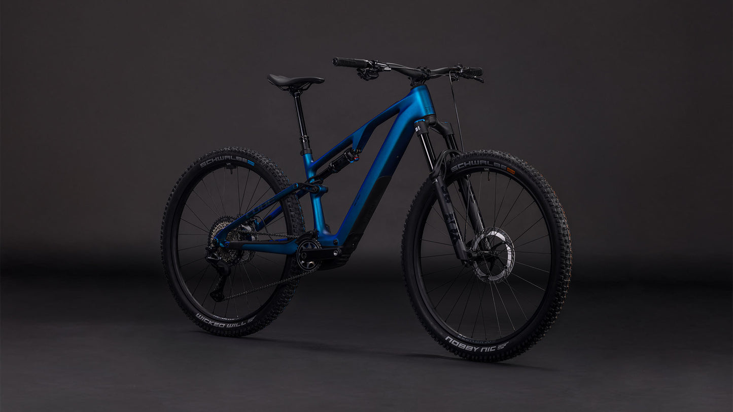 Das CUBE AMS Hybrid ONE44 C:68X SLX 400X nebula'n'black 2026, ein modernes, blau-schwarzes, vollgefedertes Mountainbike mit dicken Reifen, Scheibenbremsen und einem stabilen C:68X Carbonrahmen, steht vor einem dunklen, leicht nach rechts geneigten Hintergrund.