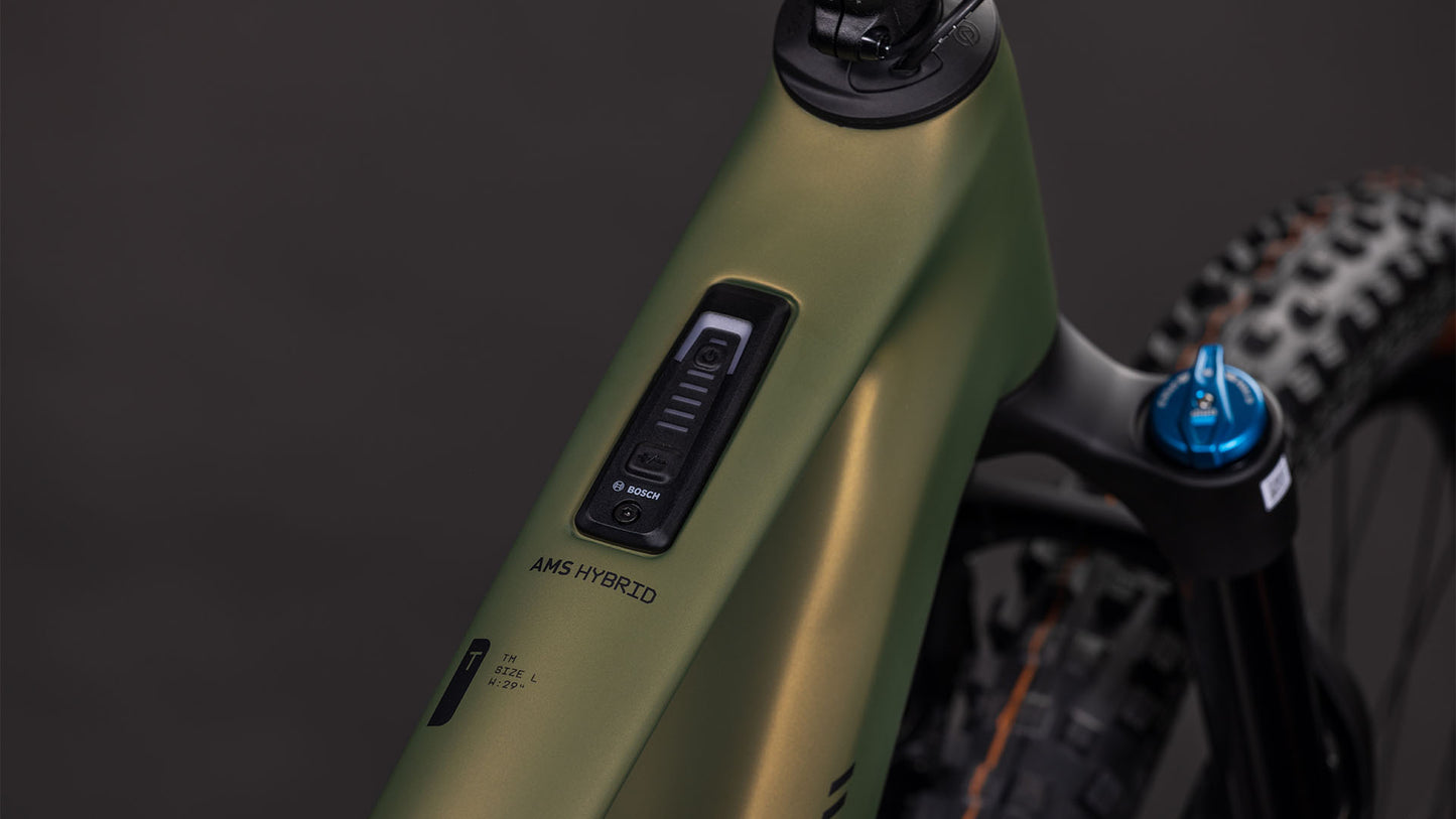 Nahaufnahme eines CUBE AMS Hybrid ONE44 C:68X TM 400X reedgreen'n'matrix 2026 Rahmens mit dem Bosch SX Motor Bedienfeld mit der Aufschrift AMS HYBRID und einem Teil der Fox Fahrwerk Federgabel mit einem blauen Einstellknopf.