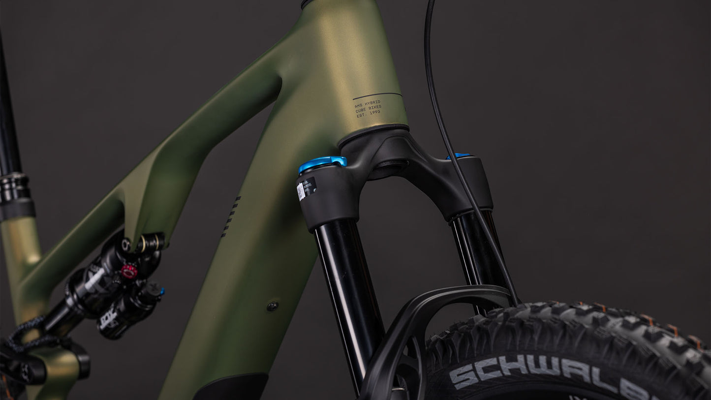 Nahaufnahme des CUBE AMS Hybrid ONE44 C:68X TM 400X reedgreen'n'matrix (2026) Rahmens, die das mattgrüne Finish, die Federgabel, den Stoßdämpfer und den Schwalbe-Reifen vor einem dunklen Hintergrund zeigt.