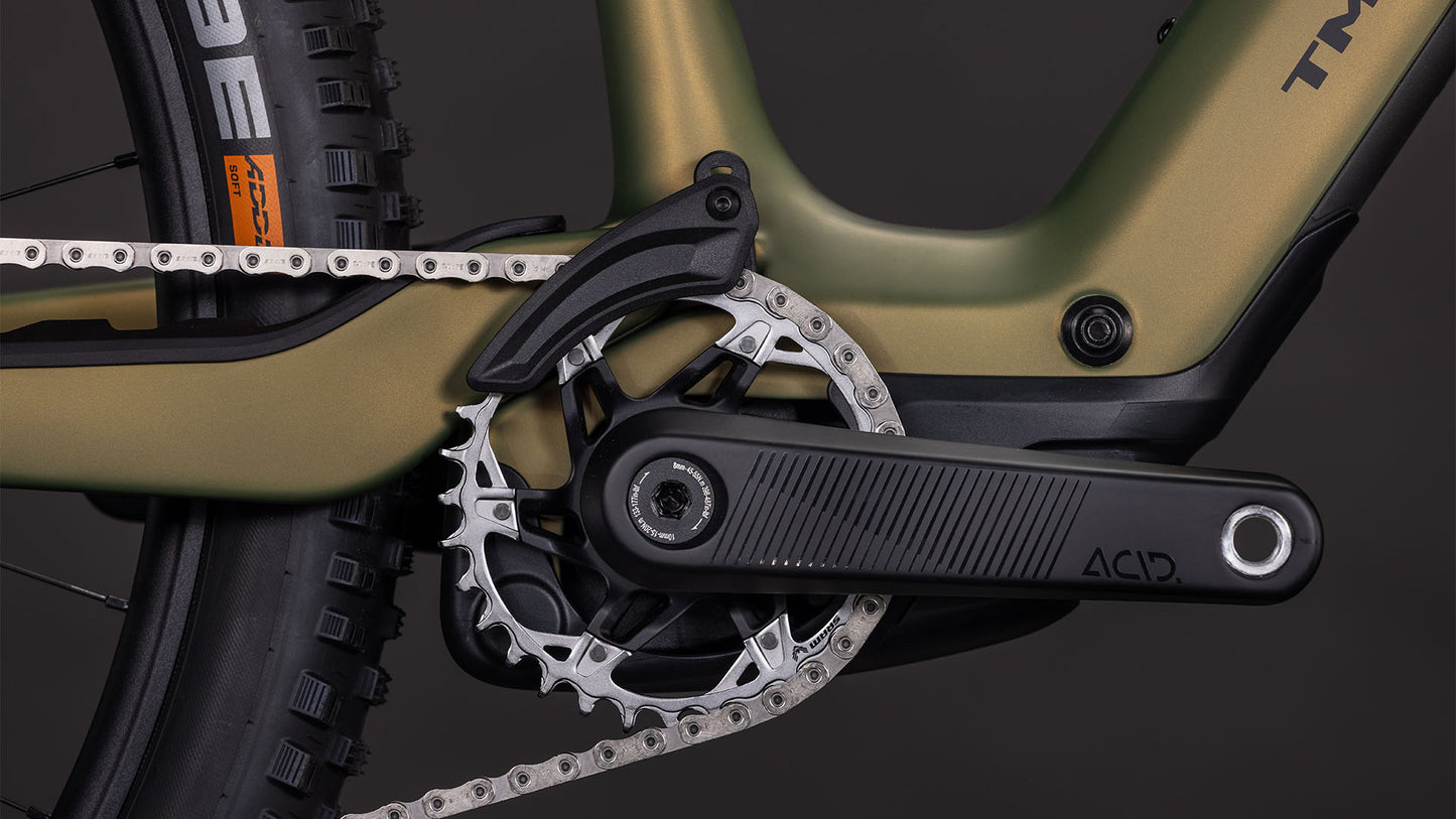 Nahaufnahme der CUBE AMS Hybrid ONE44 C:68X TM 400X Kurbelgarnitur und des Kettenblatts mit schwarzem ACID-Kurbelarm, metallischer Kette und orangefarbenem Hinterradreifen, der die C:68X Carbon-Technologie vor einem dunklen Hintergrund hervorhebt.