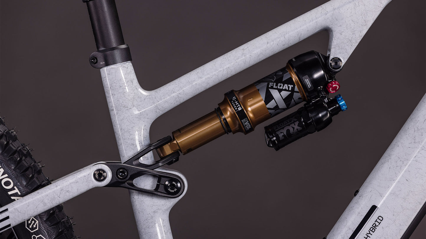 Nahaufnahme der Hinterradaufhängung des CUBE AMS Hybrid ONE44 C:68X SUPER TM 400X. Hervorzuheben sind der FOX Float X-Dämpfer am weißen Carbonrahmen, die sichtbaren Einstellknöpfe und ein Teil des Hinterrads.