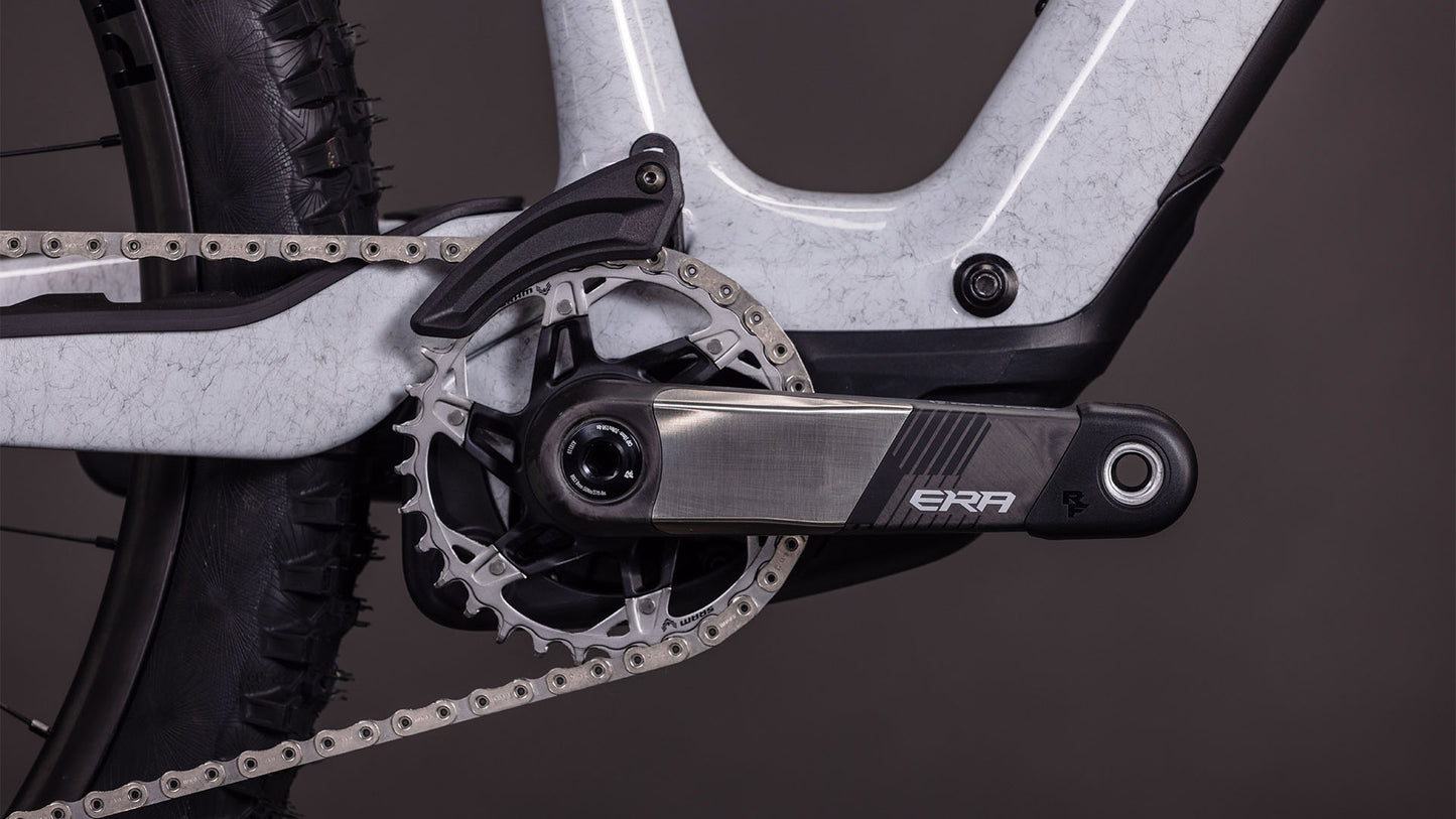 Nahaufnahme einer CUBE Cube AMS Hybrid ONE44 C:68X SUPER TM 400X Kurbelgarnitur und eines Pedalarms, die das Kettenblatt, die Kette und einen Teil des Carbonrahmens in foggrey'n'fibre 2026 vor einem dunklen Hintergrund zeigen.