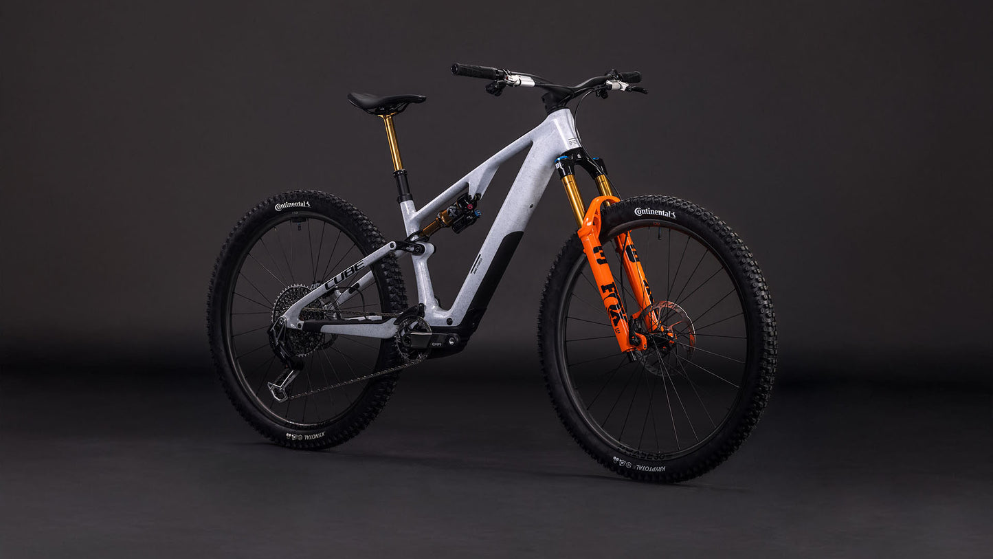 Das CUBE AMS Hybrid ONE44 C:68X SUPER TM 400X foggrey'n'fibre 2026 ist ein modernes, vollgefedertes All-Mountain-Bike mit einem nebelgrauen Carbonrahmen, schwarzen Laufrädern und einer orangefarbenen Vorderradgabel, das vor einem dunklen Studiohintergrund gezeigt wird.