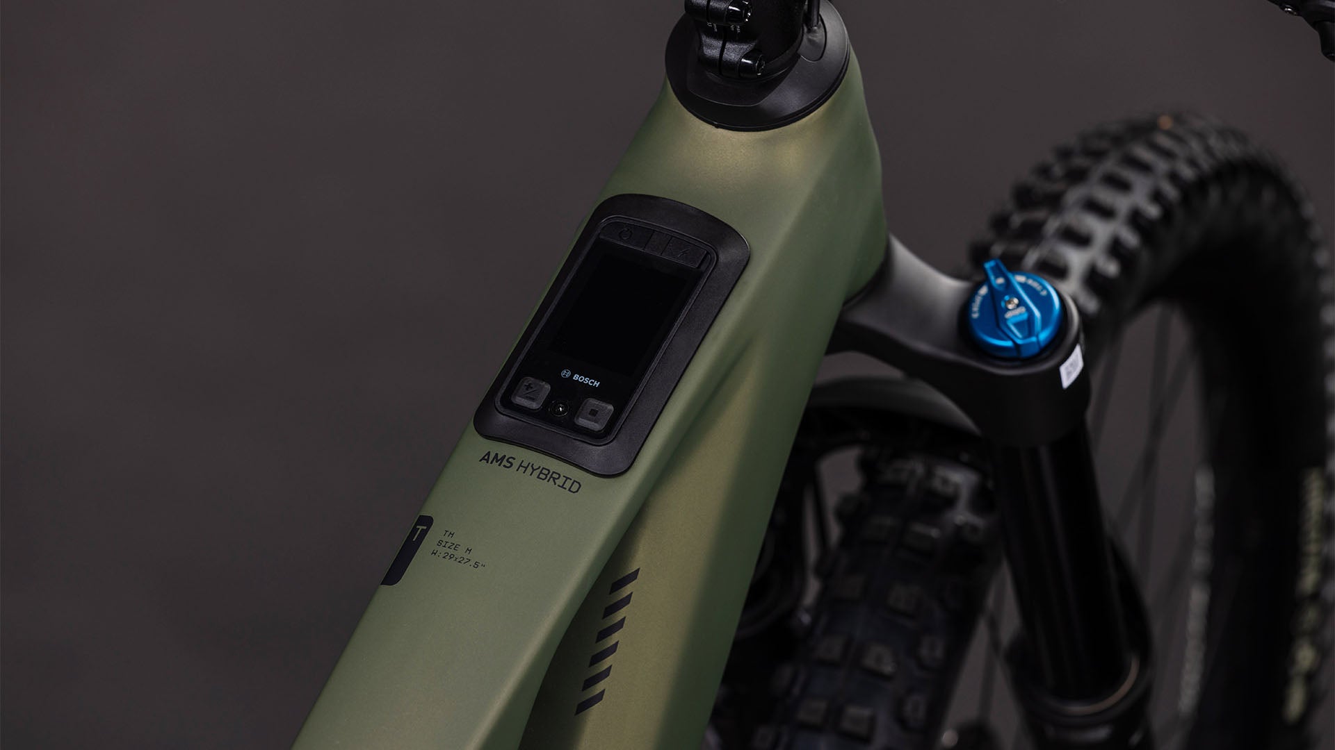 Nahaufnahme des CUBE AMS Hybrid 177 C:62 TM 600X reedgreen'n'matrix 2026: Man sieht den mattgrünen Carbonrahmen, die Digitalanzeige des Bosch CX-Motors am Lenker, die Federgabel und einen Teil des knorrigen Vorderreifens.