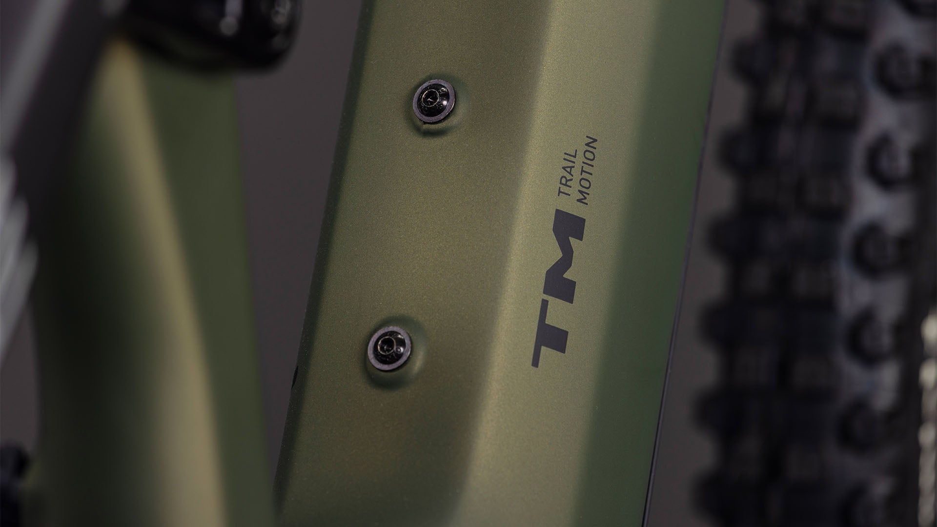 Nahaufnahme eines CUBE AMS Hybrid 177 C:62 TM 600X reedgreen'n'matrix 2026 Rahmens mit "Trail Motion" Aufdruck, zwei Befestigungsschrauben, einem sichtbaren Fahrradreifen und angetrieben von einem Bosch CX Motor für höchste E-Mountainbike Performance.