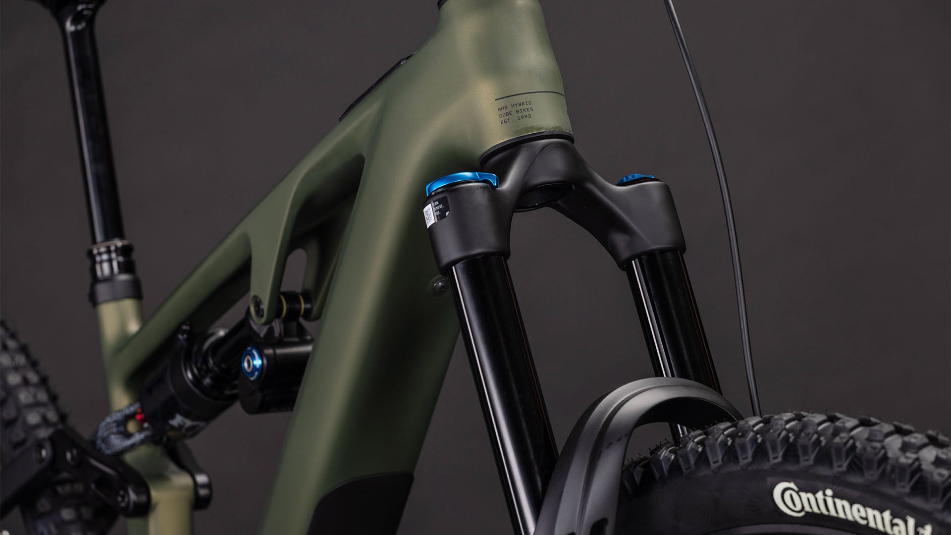 Nahaufnahme der vorderen Federgabel eines CUBE AMS Hybrid 177 C:62 TM 600X reedgreen'n'matrix 2026 E-MTB, des mattgrünen und schwarzen Rahmens und eines Continental-Vorderreifens, alles vor einem dunklen Hintergrund.