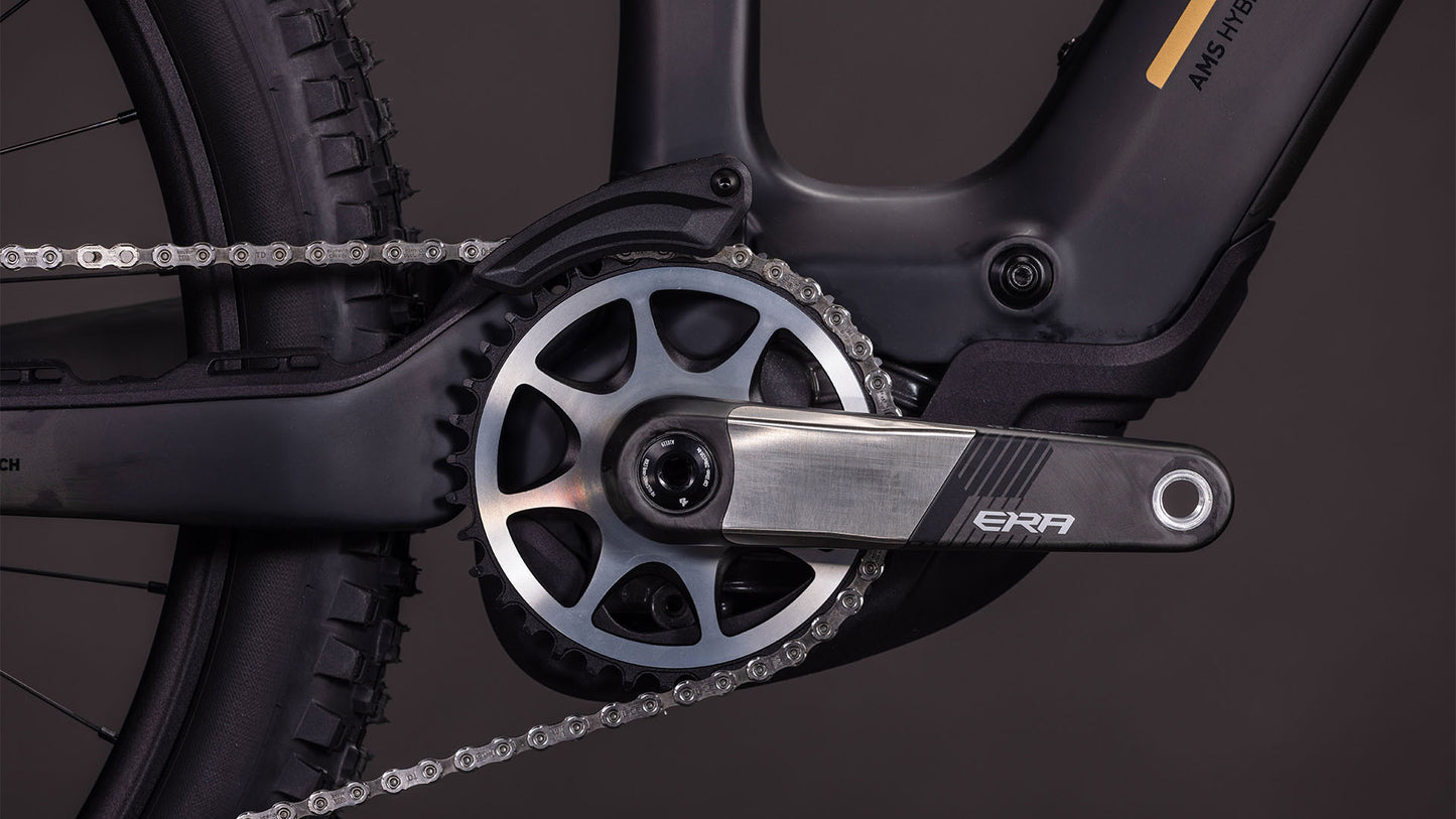 Nahaufnahme der CUBE AMS Hybrid 177 C:62 AT 600X-Kurbelgarnitur und des Kettenblatts mit ERA-Kurbelarm, Shimano XT Di2-Antrieb, Kette und Hinterradreifen vor einem dunklen Hintergrund.