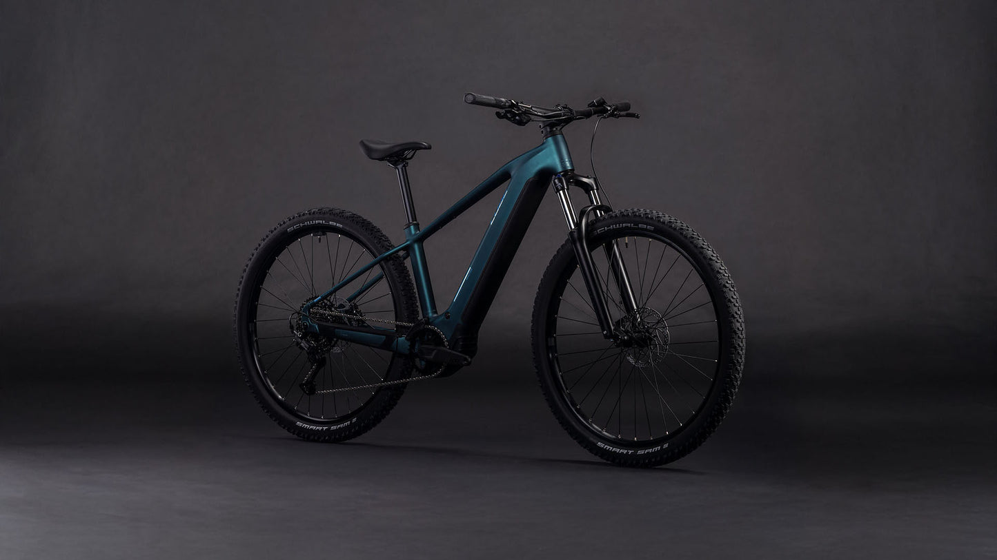 Das CUBE Reaction Hybrid ONE 800 royalgreen'n'prism 2026 mit dicken Reifen, einem schlanken Rahmen und einem leistungsstarken Bosch-Motor wird vor einem dunklen, neutralen Hintergrund präsentiert.