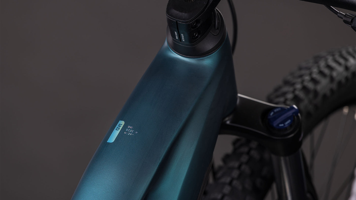 Nahaufnahme des CUBE Reaction Hybrid ONE 800 royalgreen'n'prism Trapeze 2026, die den Metallrahmen, die Vorderradgabel, die kompakte Digitalanzeige am Oberrohr und einen Teil des Vorderradreifens vor einem dunklen Hintergrund zeigt. Ausgestattet mit einem 800 Wh Akku für längere Fahrten.