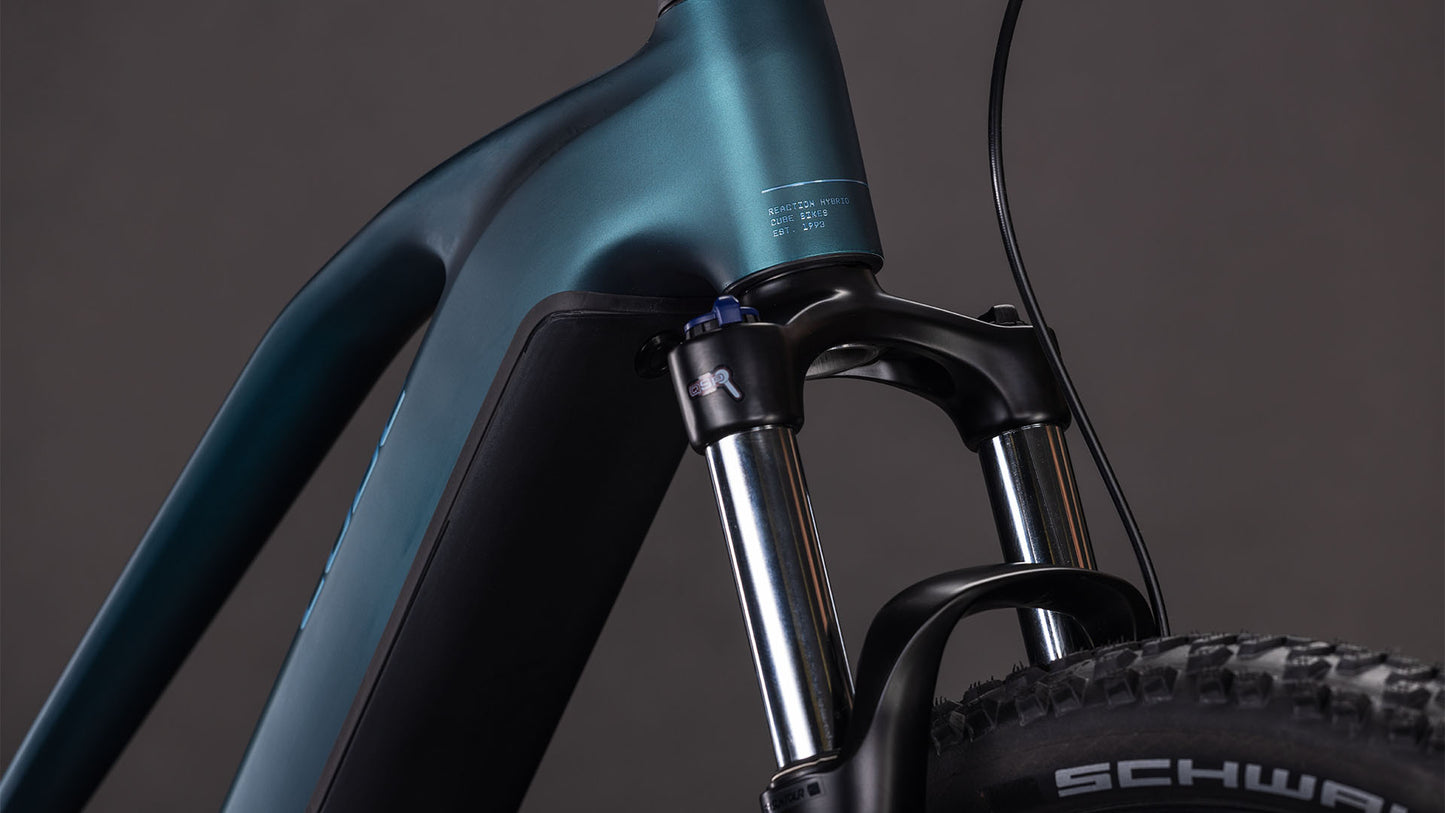 Nahaufnahme des CUBE Reaction Hybrid ONE 800 Trapeze 2026 in royalgreen'n'prism, die die vordere Federgabel, den Bosch-Motor, den Stoßdämpfer und einen Teil des Reifens vor einem dunklen Hintergrund zeigt.