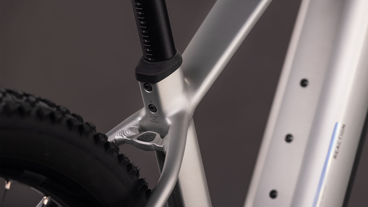 Nahaufnahme des CUBE Reaction Hybrid ONE 800 sleekgrey'n'prism 2026-Rahmens. Hervorzuheben sind die Sattelstütze (mit Messskala), das Sitzrohr, der Hinterreifen, das Oberrohr und die sichtbaren Schrauben.