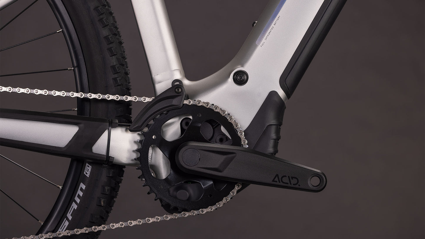 Nahaufnahme eines CUBE Reaction Hybrid ONE 800 sleekgrey'n'prism 2026 Kurbelsatz, Kette und Rahmen mit ACID-gekennzeichnetem Pedalarm und sichtbarem Bosch-Motor. Der dunkle Hintergrund betont die herausragenden Komponenten dieses E-Bikes.