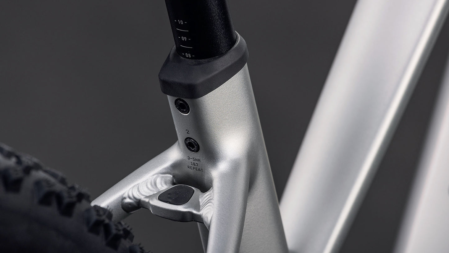 Nahaufnahme des CUBE Reaction Hybrid ONE 800 sleekgrey'n'prism Trapeze 2026 Rahmens, wobei das Sitzrohr, die Sattelstütze und der Hinterreifen mit sichtbaren Schrauben und Einstellmarkierungen vor einem dunklen Hintergrund hervorgehoben werden.