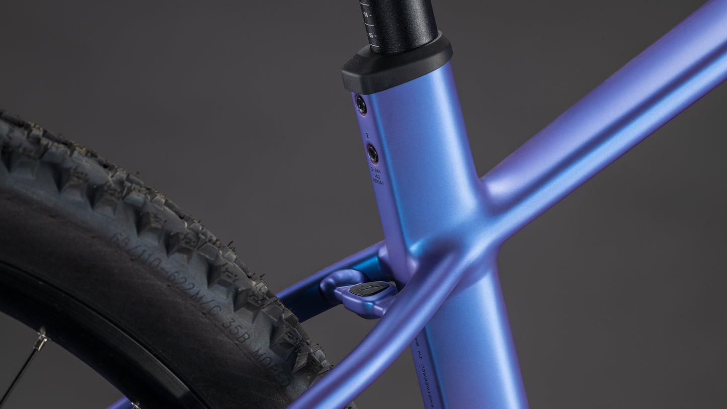 Die Nahaufnahme des CUBE Reaction Hybrid ONE 800 blueiris'n'reflect 2026 zeigt den Metallrahmen, das Sitzrohr, den Bosch-Motor und den hinteren Noppenreifen am Rahmenübergang vor einem dunklen Hintergrund.