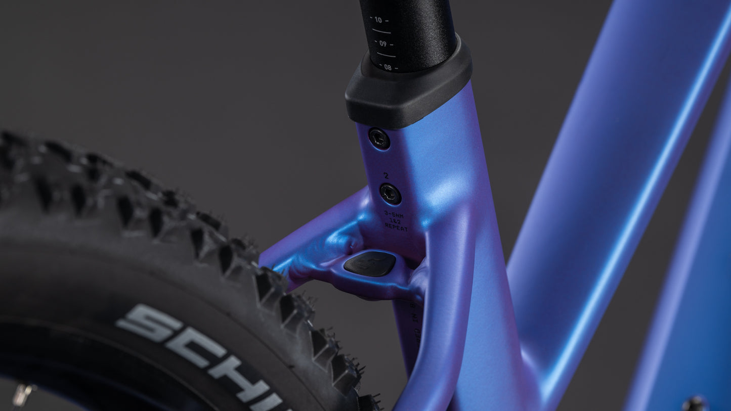 Nahaufnahme des CUBE Reaction Hybrid ONE 800 blueiris'n'reflect Trapeze 2026 Rahmens mit Sattelstütze, Schwalbe-Hinterradreifen, Einstellschrauben und Bosch-Motor - alles vor einem dunklen Hintergrund.