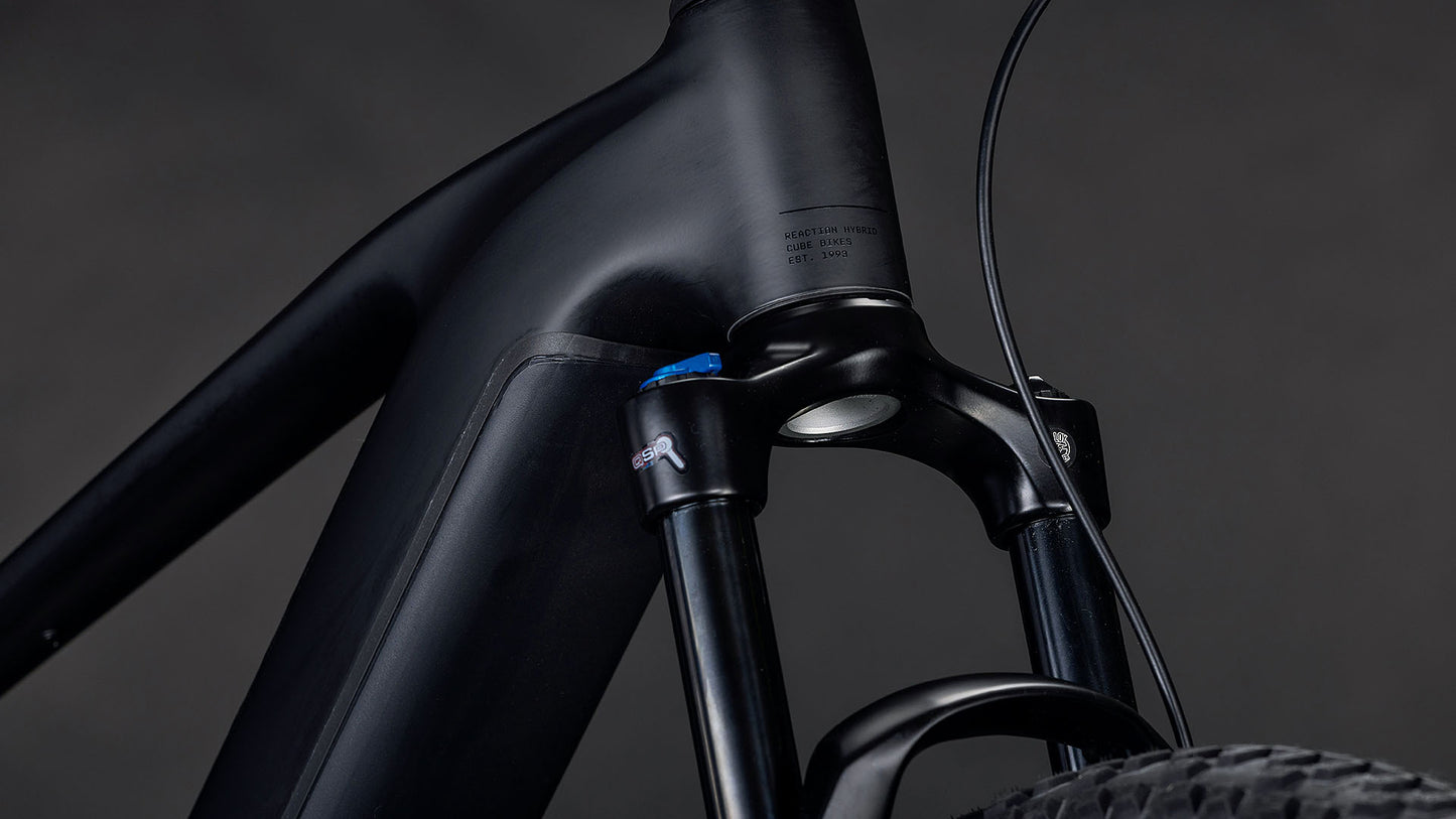 Die Nahaufnahme des CUBE Reaction Hybrid Pro 800 blackline 2026 E-Mountainbike-Rahmens zeigt die mattschwarze Federgabel, das Steuerrohr, das Vorderradsegment, die sichtbaren Kabel und den Bosch CX-Antrieb vor einem dunklen Hintergrund.