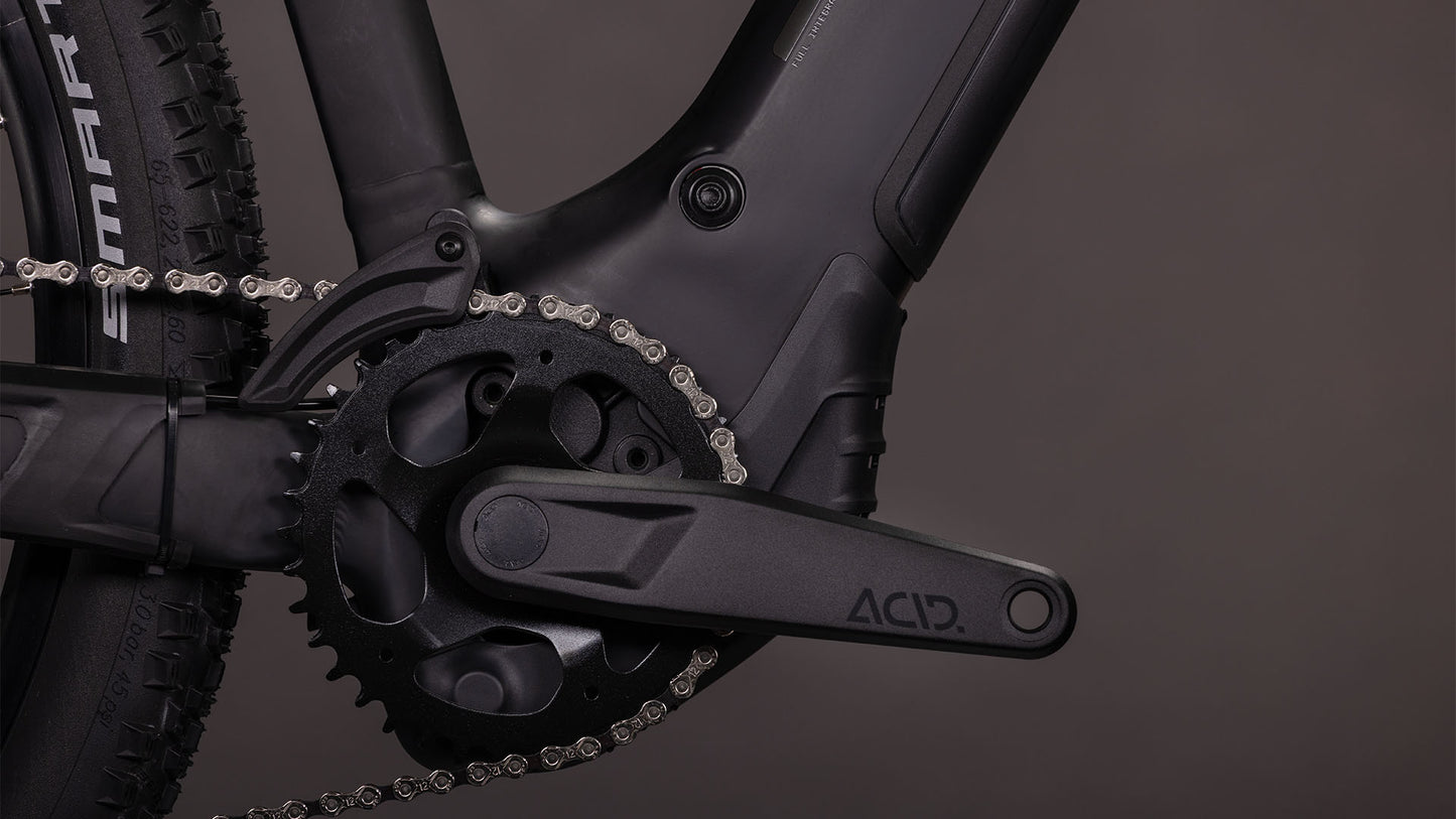 Nahaufnahme der CUBE Reaction Hybrid Pro 800 blackline Trapeze 2026 Kurbelgarnitur, des Kettenblatts und des ACID-Pedalarms. Hervorzuheben sind die Details des Bosch CX-Antriebssystems und des Antriebsstrangs, wobei ein Teil des Hinterrads sichtbar ist.