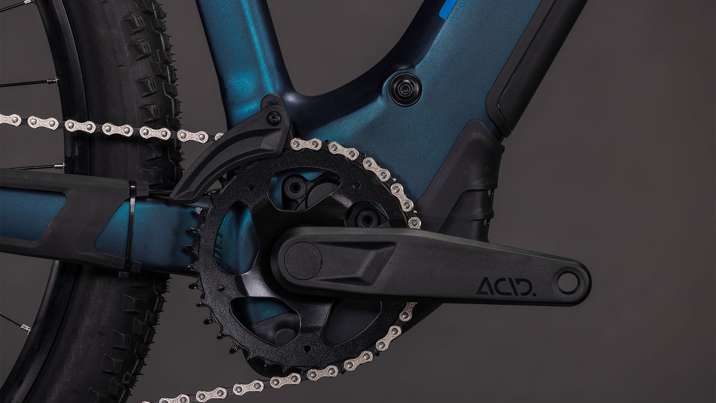 Nahaufnahme einer CUBE-Kurbelgarnitur mit dem Schriftzug "ACID" auf dem Arm, mit Blick auf Kette, Kettenblatt und Hinterrad - zu sehen am Cube Reaction Hybrid Pro 800 nebular'n'dazzle 2026 E-MTB mit 800 Wh-Akku und Bosch CX-Antrieb.