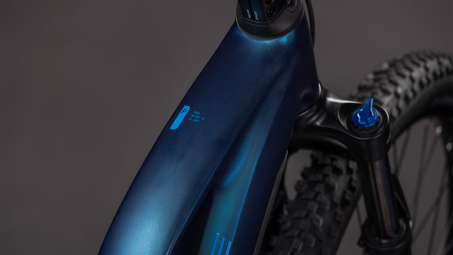 Nahaufnahme des CUBE Reaction Hybrid Pro 800 nebular'n'dazzle Trapeze 2026 Rahmens und der vorderen Federgabel, die ein kleines blaues Logo und einen Teil des Noppenreifens vor einem neutralen grauen Hintergrund zeigt.