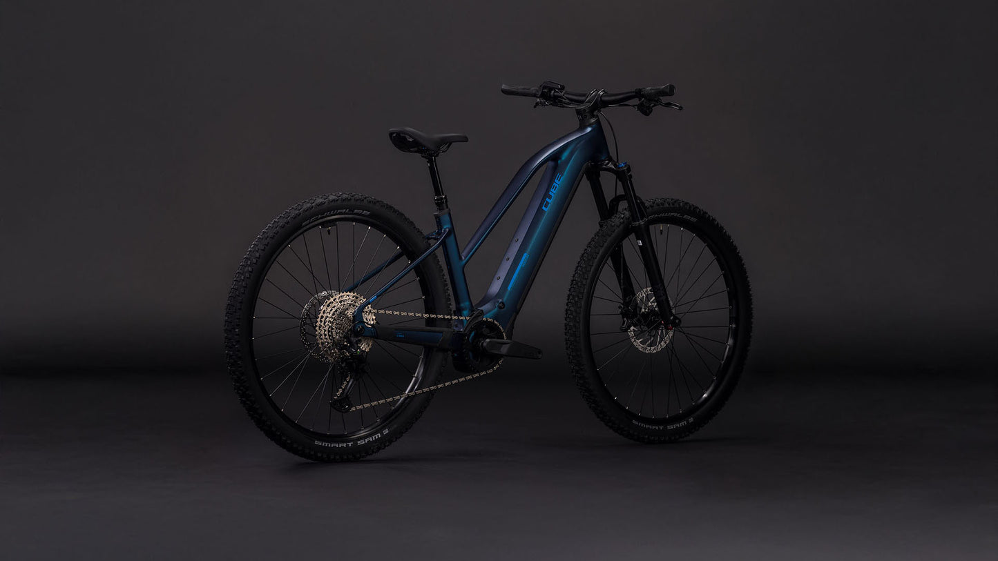 Das CUBE Reaction Hybrid Pro 800 nebular'n'dazzle Trapeze 2026 ist ein blaues E-Mountainbike mit dicken Reifen, Scheibenbremsen, Durchstiegsrahmen und einem 800-Wh-Akku am Unterrohr, der vor einem dunklen Hintergrund steht.
