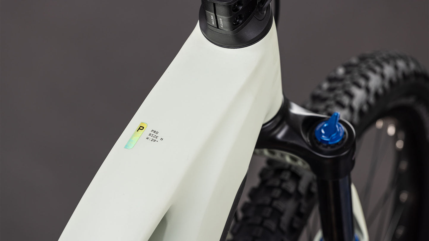 Nahaufnahme des CUBE Reaction Hybrid Pro 800 desertstone'n'driedherbs Trapeze 2026 Rahmens, mit Hervorhebung des Oberrohrs, der Federgabel und eines Aufklebers mit Text und einer Grafik; der Hintergrund ist unscharf.