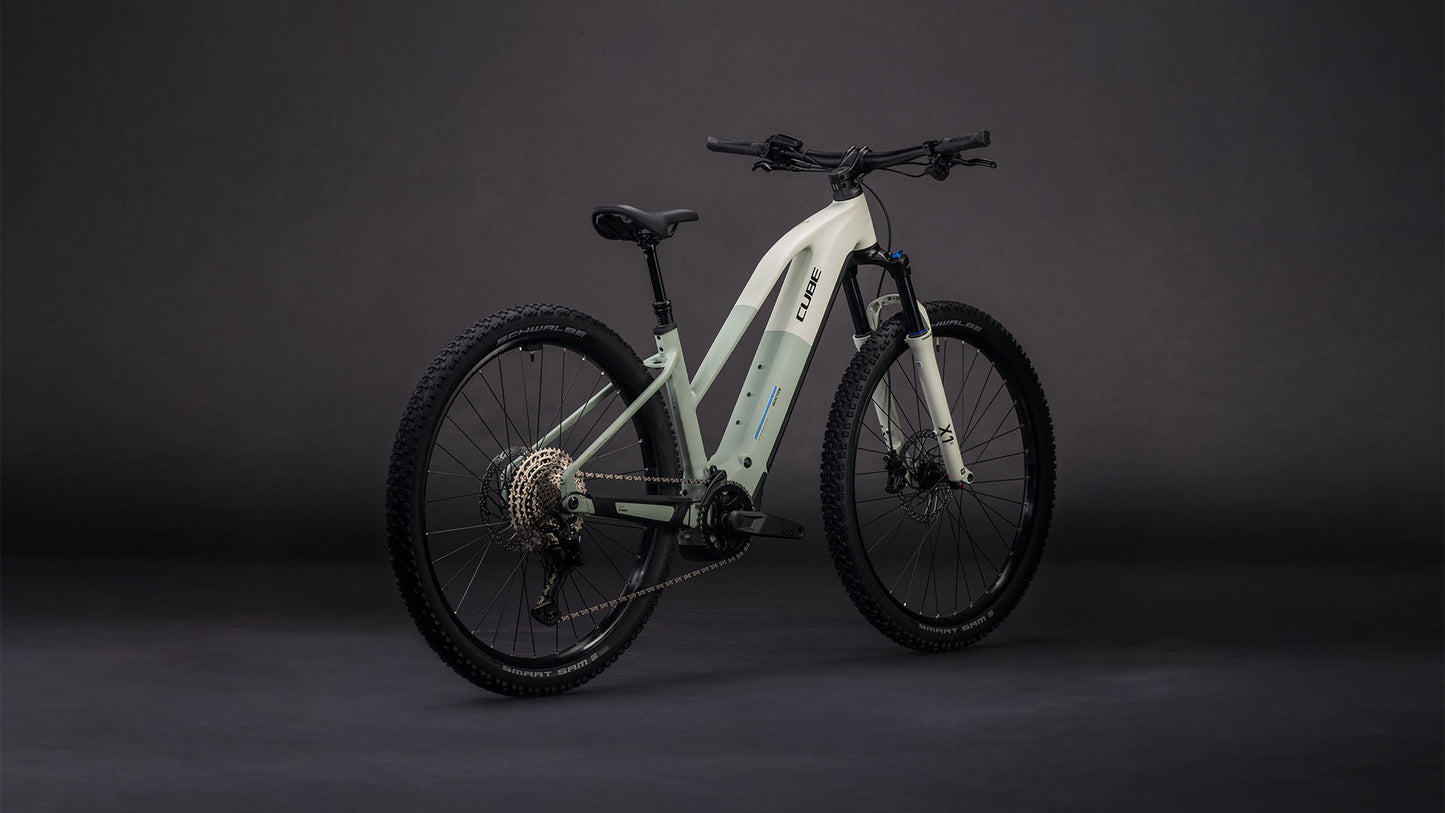 Das CUBE Reaction Hybrid Pro 800 desertstone'n'driedherbs Trapeze 2026 ist ein modernes E-Mountainbike mit dicken Reifen, integriertem 800-Wh-Akku und Vorderradfederung, abgebildet auf einem Hintergrund mit dunklem Farbverlauf.