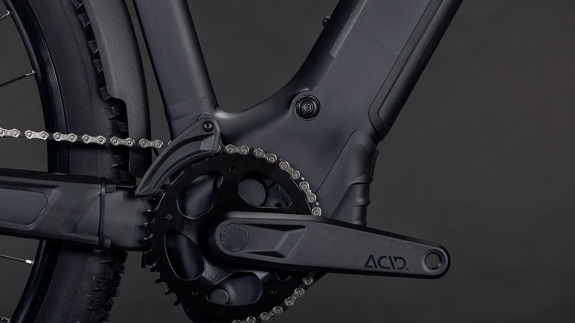 Nahaufnahme einer CUBE Reaction Hybrid Pro 800 FE blackline 2026 E-Bike Kurbelgarnitur und Kettenblatt, mit ACID-gekennzeichnetem Kurbelarm, Rahmen, Kette und Hinterradreifen sichtbar. Mit Bosch CX-Motor für starke Leistung vor dunklem Hintergrund.