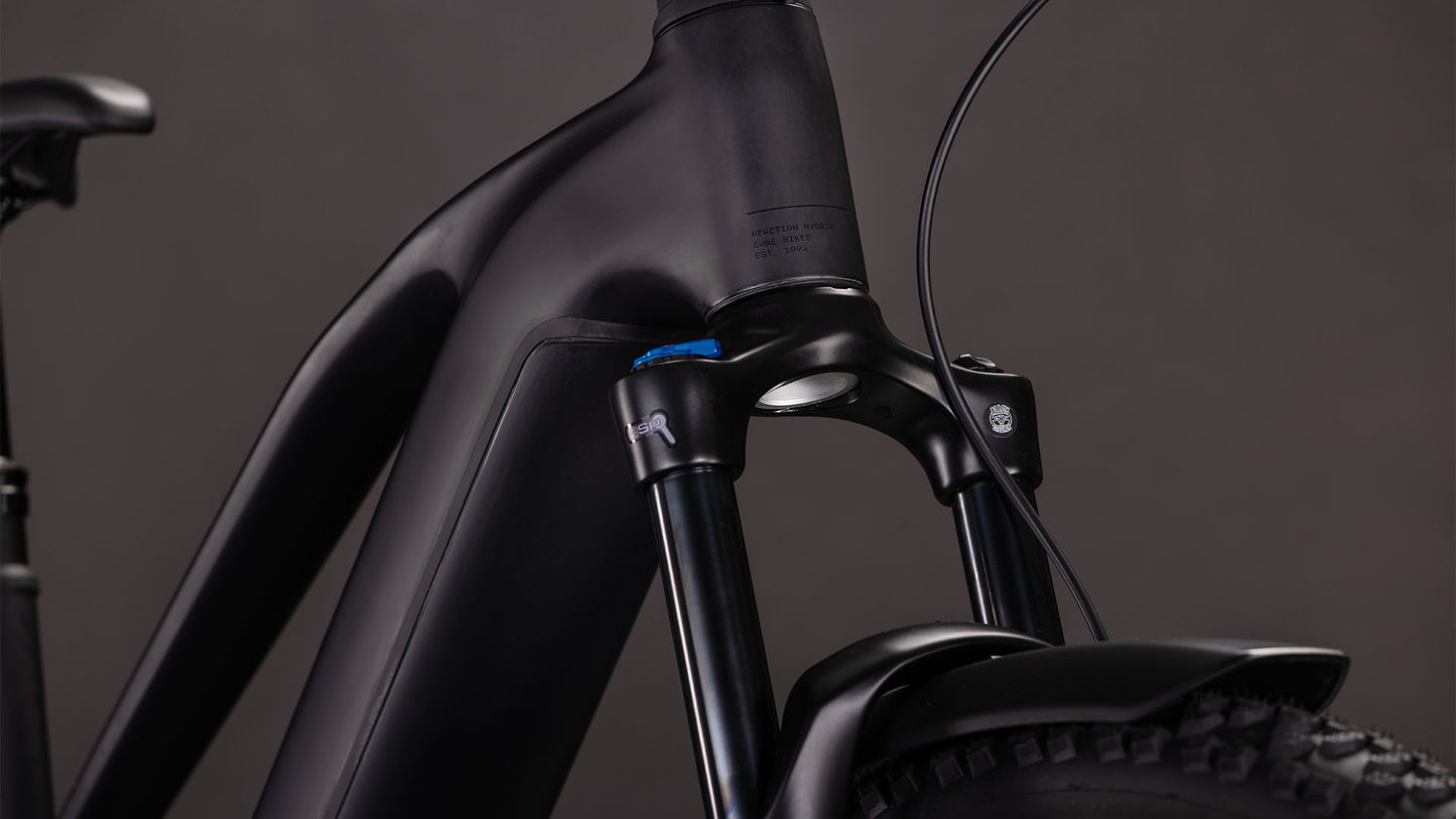Nahaufnahme des CUBE Reaction Hybrid Pro 800 FE blackline Trapeze 2026, die den mattschwarzen Rahmen, die Federgabel, die Lenkerkabel und den Vorderreifen zeigt und den Bosch CX Motor vor einem dunklen Hintergrund in den Mittelpunkt stellt.