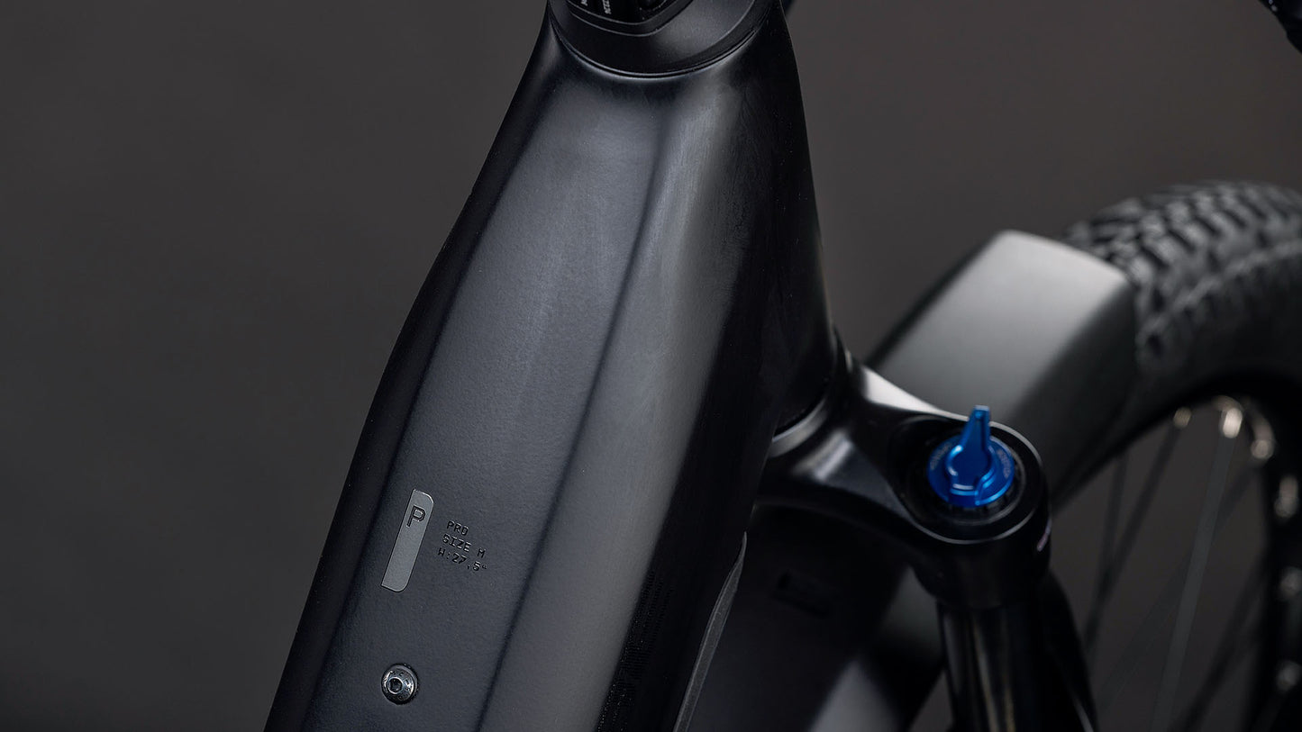 Nahaufnahme des CUBE Reaction Hybrid Pro 800 FE blackline Easy Entry 2026 Rahmens, die das Batteriefach des Bosch CX-Motors mit Knopf und Anzeige sowie ein Detail der Vorderradaufhängung mit einem blauen Einstellknopf zeigt.
