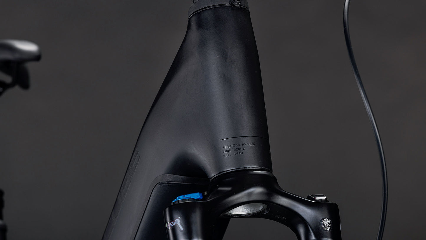Nahaufnahme des CUBE Reaction Hybrid Pro 800 FE blackline Easy Entry 2026 mit mattschwarzem Rahmen und Federgabel. Glatte Linien, minimalistisches Design, ein sichtbares Kabel, Satteldetails und eine hochwertige Shimano XT 12-fach Schaltung vor einem dunklen Hintergrund.