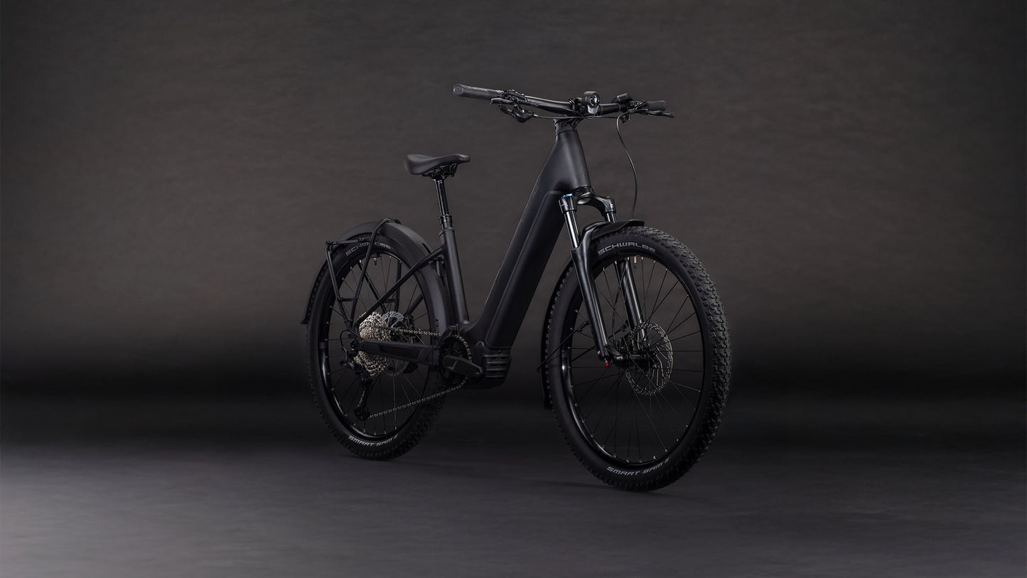 Das CUBE Reaction Hybrid Pro 800 FE blackline Easy Entry 2026, ein mattschwarzes E-Bike mit dicker Bereifung, Federgabel, Schutzblechen und Durchstiegsrahmen, besticht durch einen Bosch CX-Motor und modernes Design vor dunklem Hintergrund.