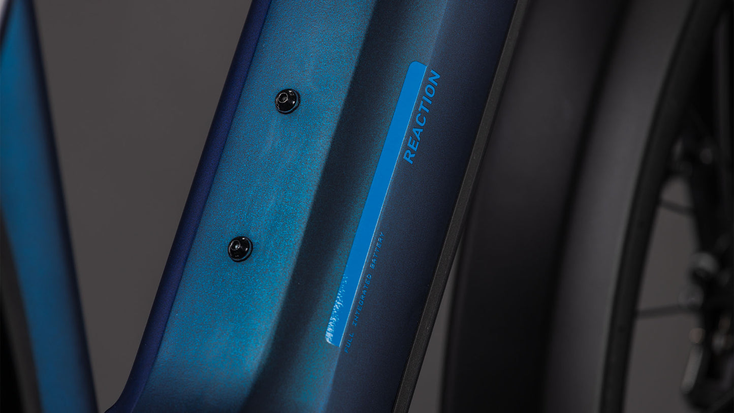 Nahaufnahme eines blauen CUBE Reaction Hybrid Pro 800 FE nebular'n'dazzle 2026 Rahmens mit zwei Befestigungslöchern und REACTION Aufdruck an der Seite, im Hintergrund ein Teil des Hinterrads und der Shimano XT Schaltung sichtbar.