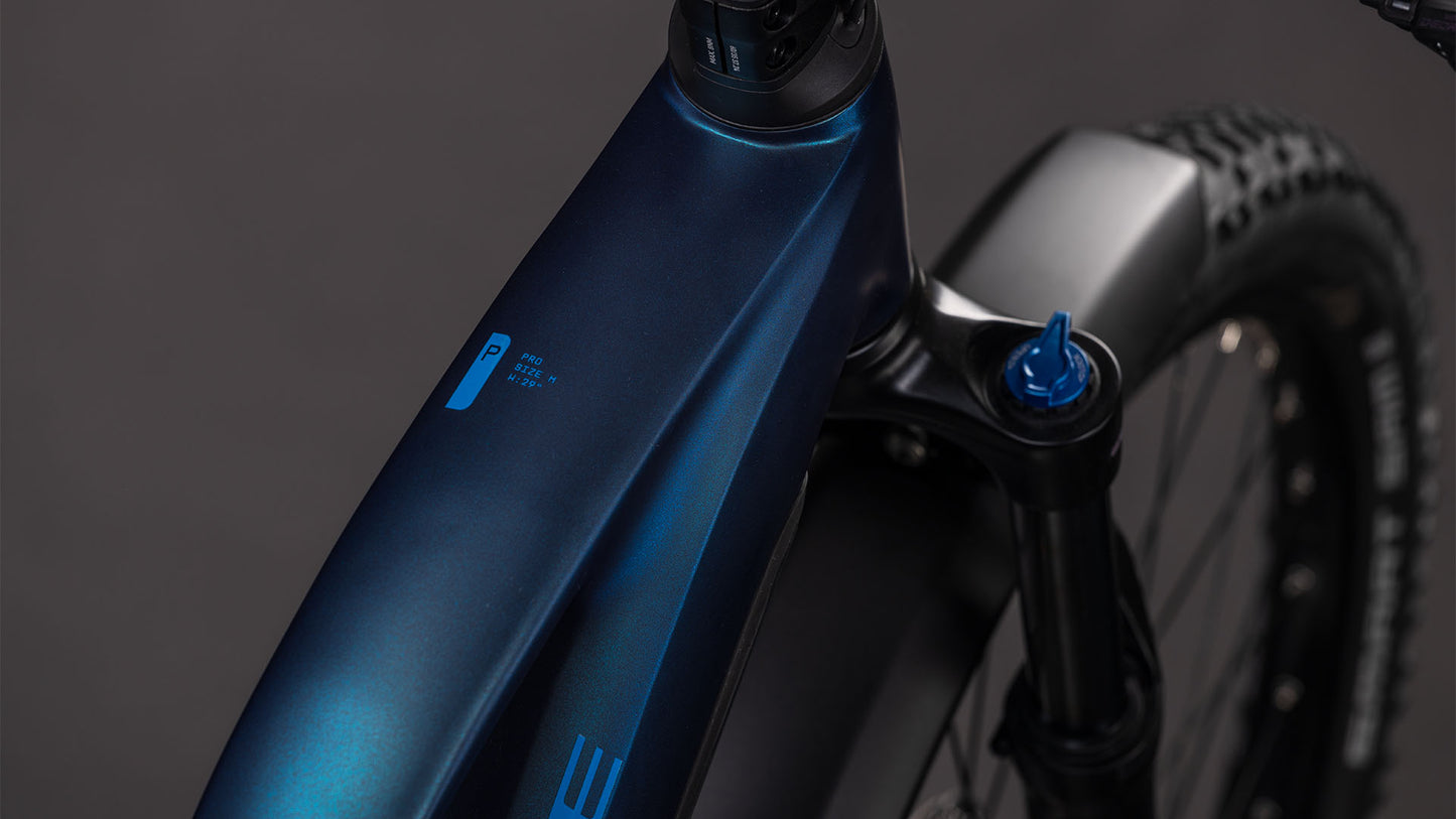 Nahaufnahme des dunkelblauen CUBE Reaction Hybrid Pro 800 FE nebular'n'dazzle Trapeze 2026 Rahmens mit Federgabel, Reifen und Batterieanzeige. Der Bosch CX-Motor verspricht eine starke Leistung. Der Hintergrund ist dunkelgrau und unscharf.