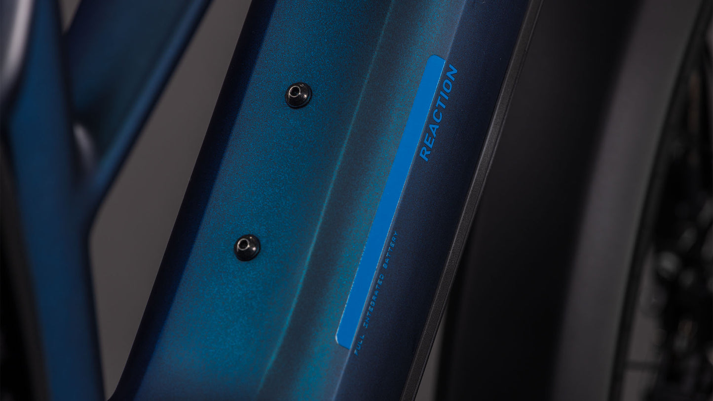 Nahaufnahme des blauen CUBE Reaction Hybrid Pro 800 FE nebular'n'dazzle Trapeze 2026 E-Bike-Rahmens mit dem Wort "REACTION" in Blau und zwei sichtbaren Schrauben; der Hintergrund ist unscharf.