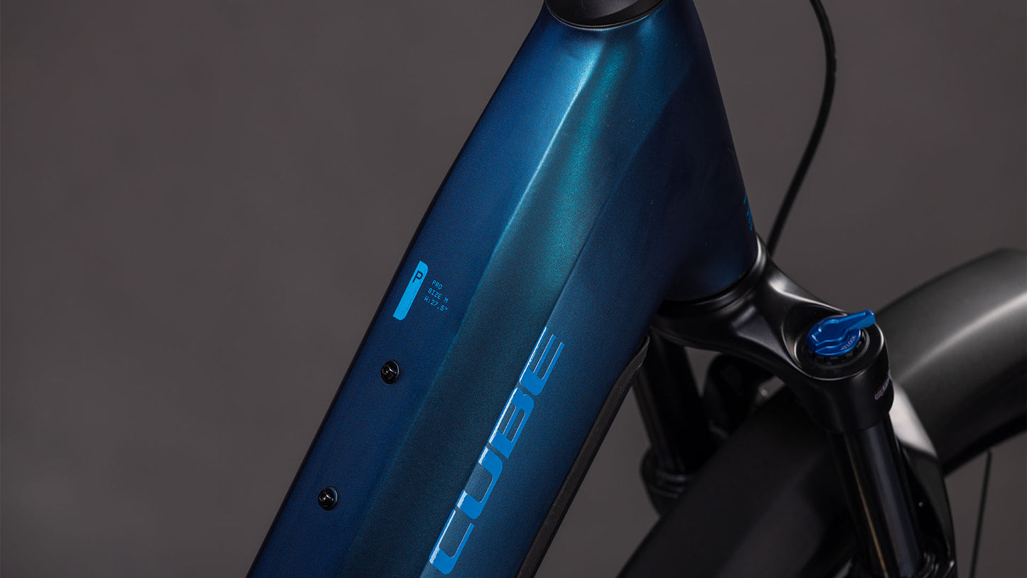 Nahaufnahme des Cube Reaction Hybrid Pro 800 FE nebular'n'dazzle Easy Entry 2026 von CUBE, die den blauen Rahmen mit Logo, Oberrohr, Vorderradgabel und Batterieanzeige hervorhebt. Das E-Bike hebt sich vor einem unscharfen grauen Hintergrund ab.