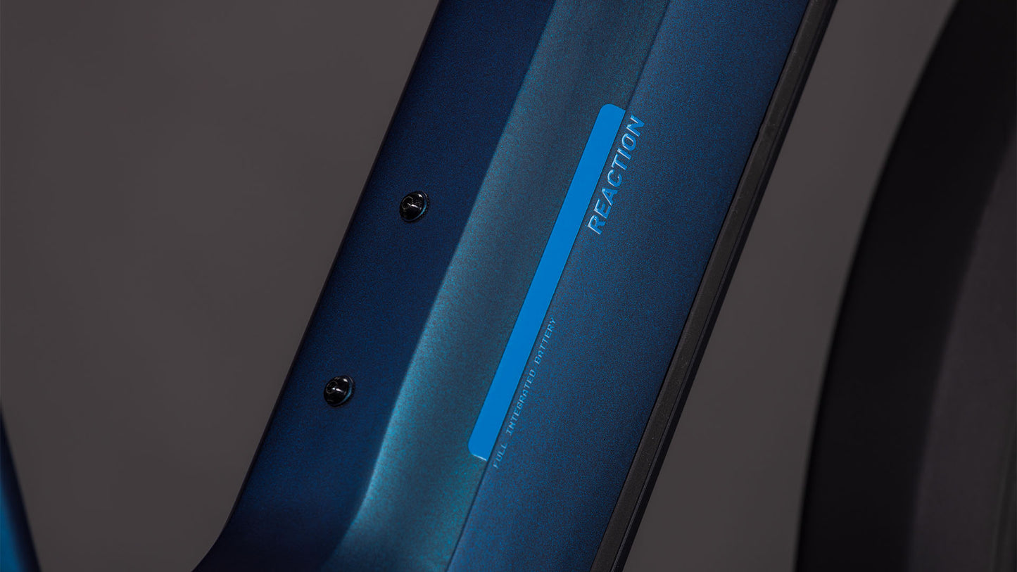 Nahaufnahme des glatten, metallischen Rahmens des CUBE Reaction Hybrid Pro 800 FE nebular'n'dazzle Easy Entry 2026 E-Bike, mit "REACTION" und kleinem blauen Aufkleber. Zwei Schrauben sind vor einem dunklen Hintergrund zu sehen.