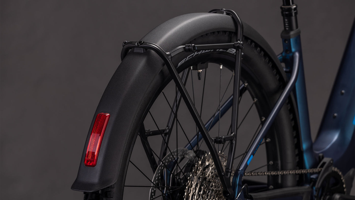 Nahaufnahme des Hinterrads des CUBE Reaction Hybrid Pro 800 FE nebular'n'dazzle Easy Entry 2026 mit schwarzem Schutzblech, rotem Reflektor, Schaltkassette und Rahmendetails, die das robuste Design von CUBE vor einem dunklen Hintergrund hervorheben.