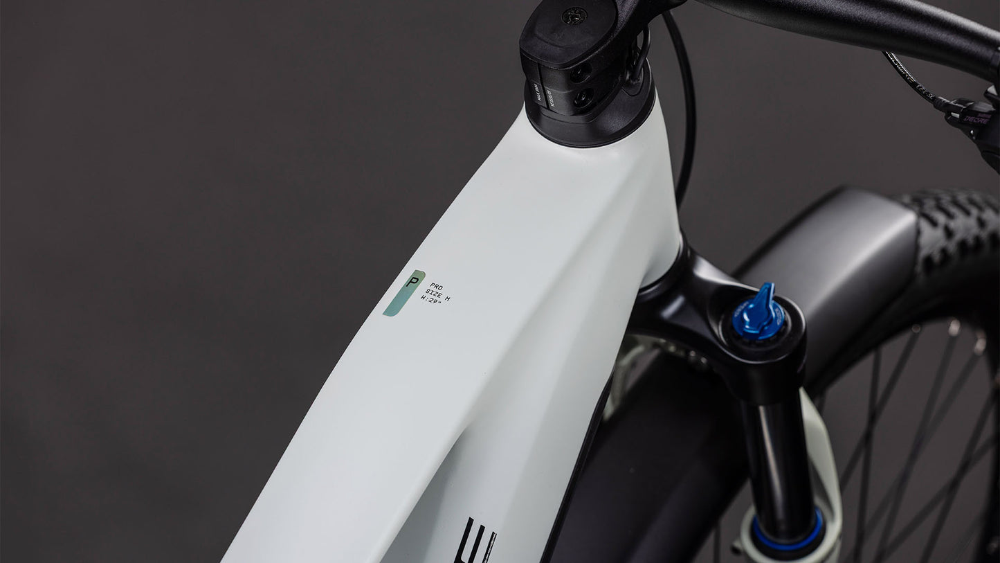 Nahaufnahme des Cube Reaction Hybrid Pro 800 FE desertstone'n'driedherbs 2026 von CUBE mit seinem modernen weißen Rahmen, der Digitalanzeige am Oberrohr, dem sichtbaren Lenker, der Federgabel und den strukturierten Reifen vor einem dunklen Hintergrund.