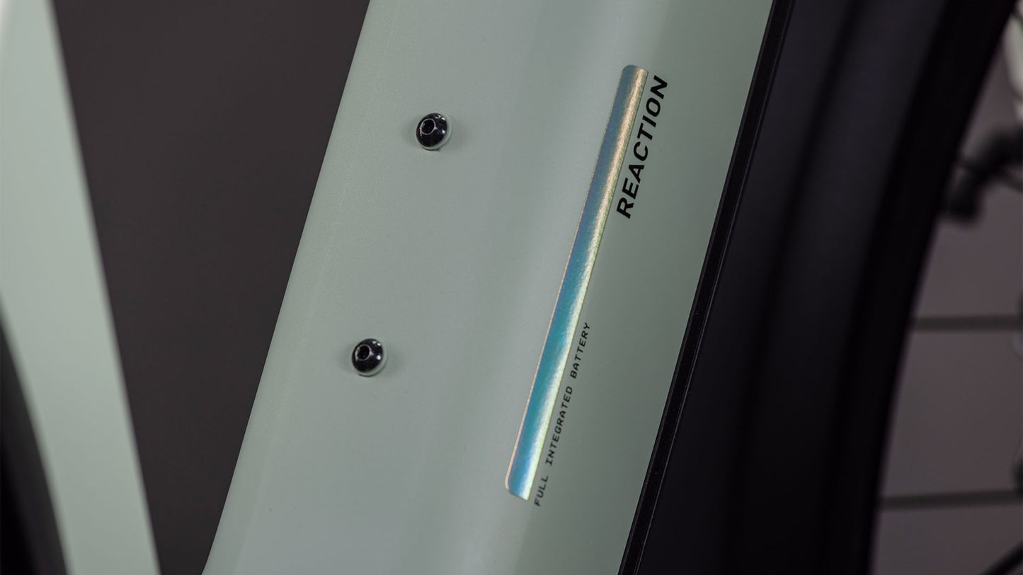 Die Nahaufnahme des CUBE Reaction Hybrid Pro 800 FE (desertstone'n'driedherbs, 2026) E-Bike-Rahmens zeigt zwei Schraubenhalterungen, die Aufschrift "REACTION" und "FULL INTEGRATED OPTICS" in der Nähe eines reflektierenden Streifens sowie Angaben zum Bosch CX-Motor am unteren Rand.