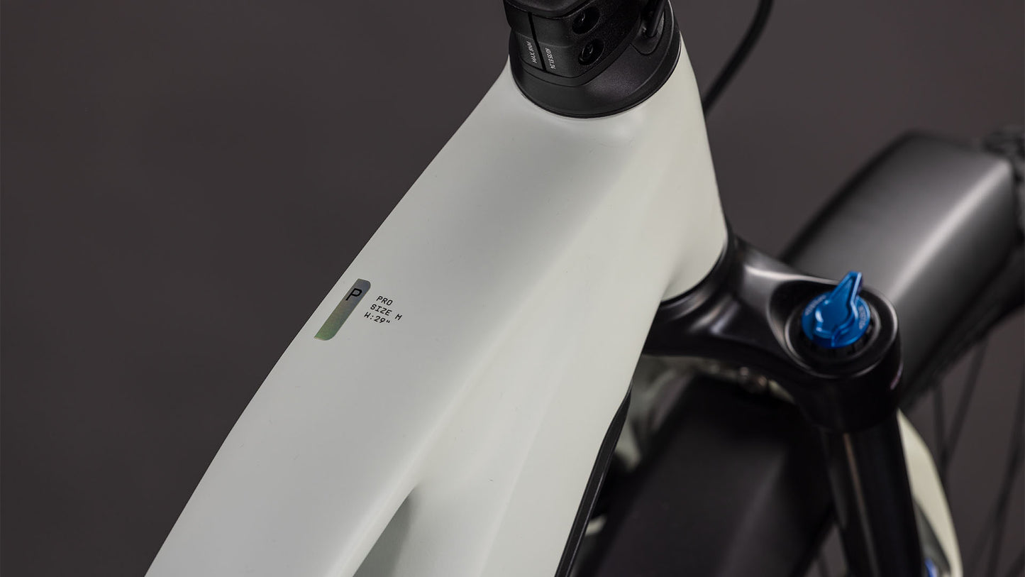 Nahaufnahme des CUBE Cube Reaction Hybrid Pro 800 FE desertstone'n'driedherbs Trapeze 2026 E-Bike-Rahmens in der Nähe des Lenkers, die eine kleine LED-Anzeige mit Akku- und Leistungsinformationen vor einem dunklen Hintergrund zeigt.