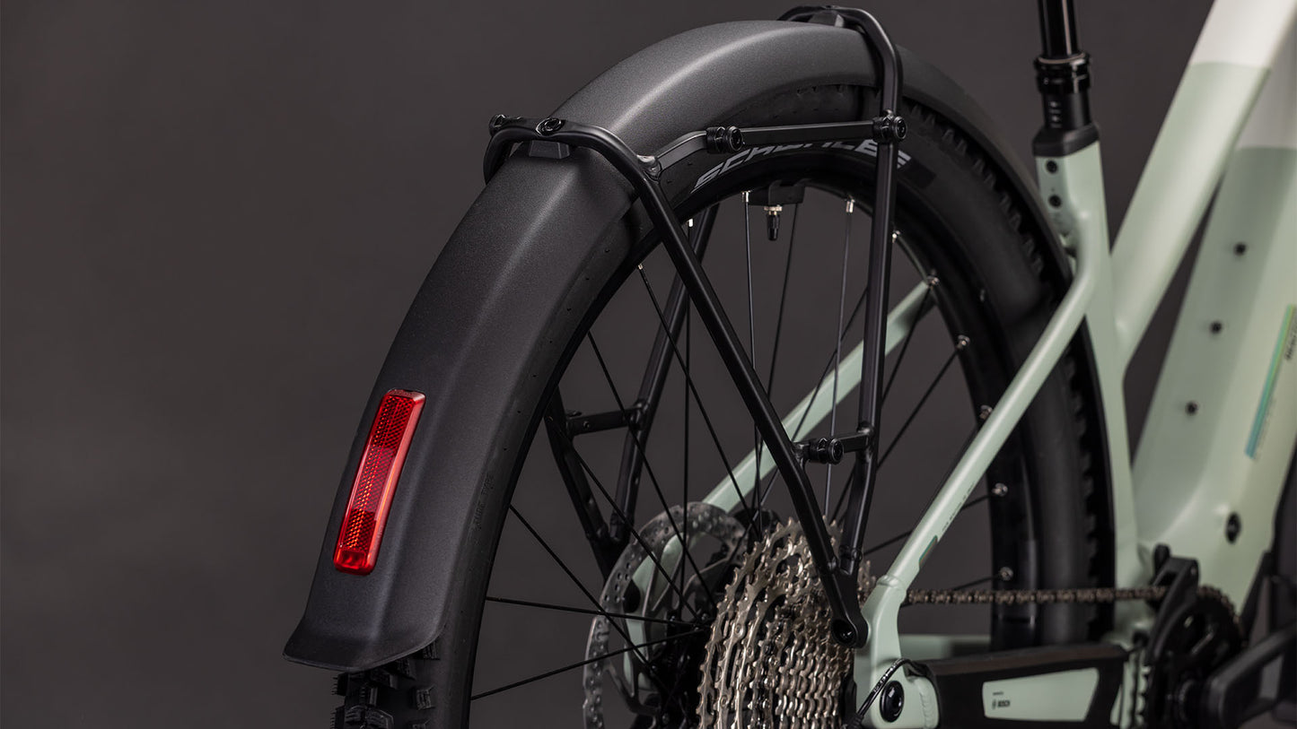 Nahaufnahme des Hinterrads des CUBE Cube Reaction Hybrid Pro 800 FE desertstone'n'driedherbs Trapeze 2026, die das schwarze Schutzblech mit rotem Reflektor, die Shimano XT 12-fach Schaltung und den E-Bike-Rahmen vor einem dunklen Hintergrund zeigt.